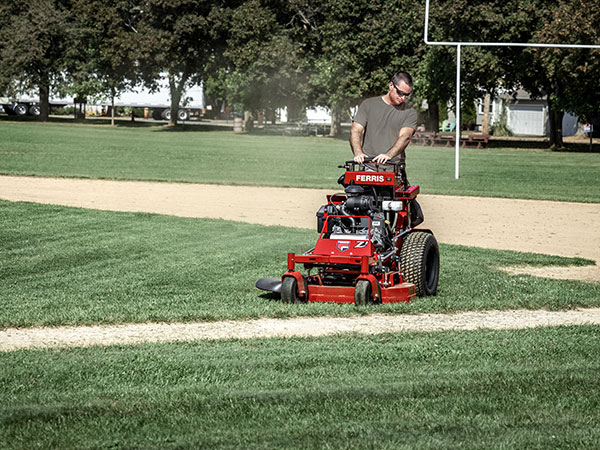 Man riding a Ferris Z1 stand on mower at baseball field.