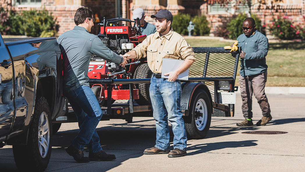 Man shaking hands with another man with Ferris mower loaded in trailer behind them