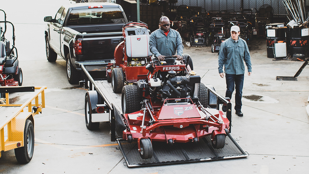 Man on stand-on mower driving it off the trailer ramp